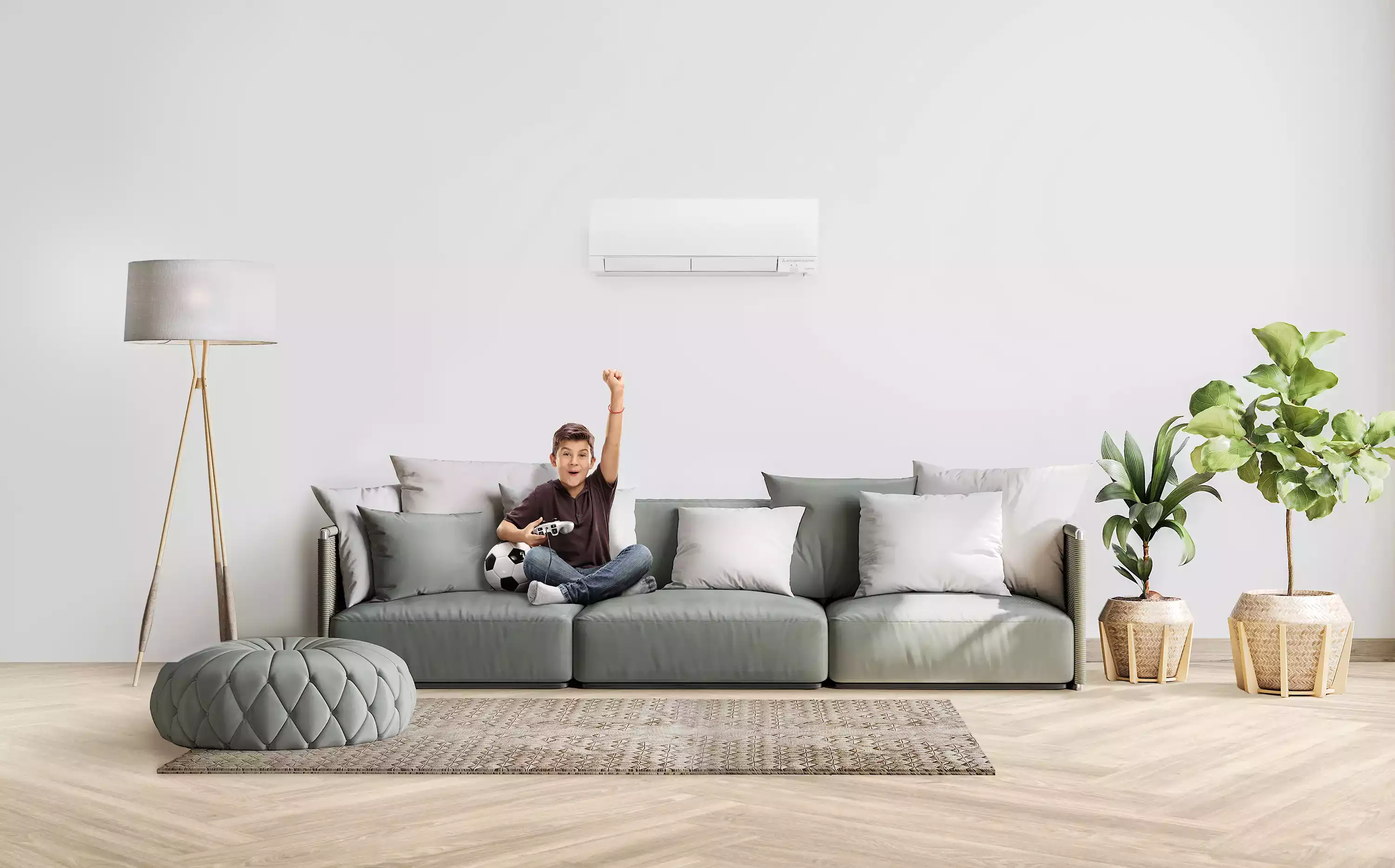 Boy sitting on a sofa, holding a video game controller, celebrating under a wall-mounted air conditioner in a modern living room.