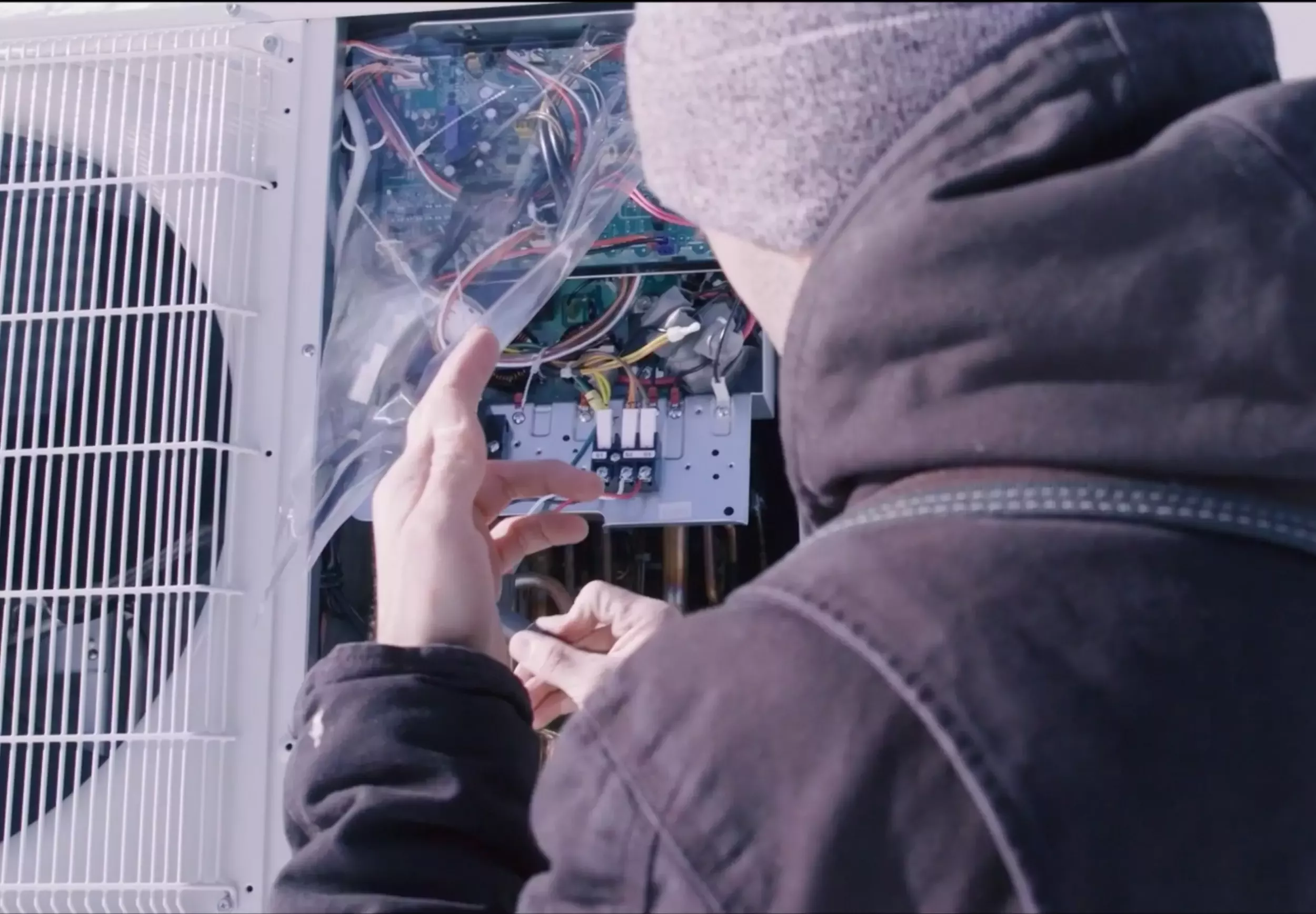 Technician working on an outdoor HVAC unit, inspecting internal wiring and components.